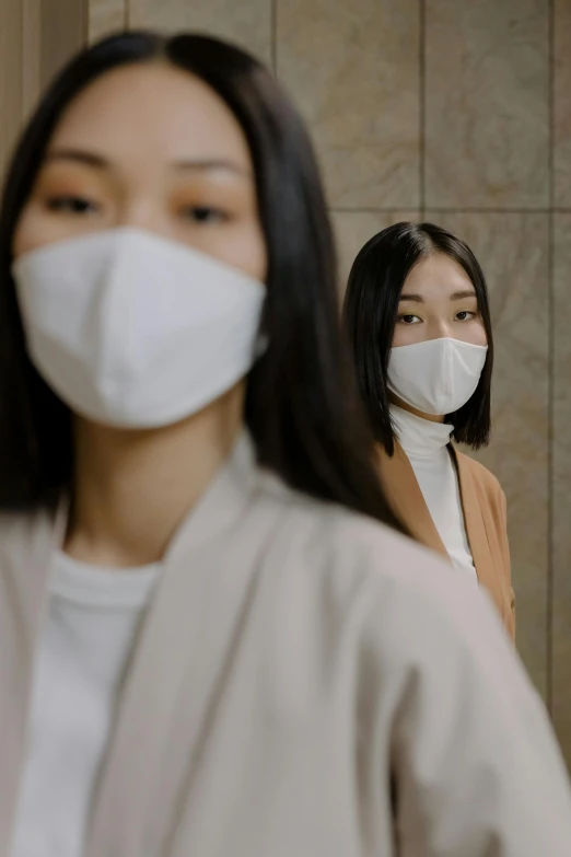 a woman standing in front of a mirror wearing a face mask, inspired by Kanō Naizen, trending on pexels, medium shot of two characters, beige, ethnicity : japanese, 2 techwear women