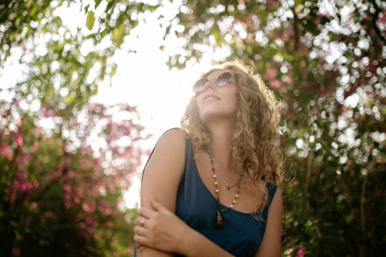 a woman in a blue dress looking up at the sky, a picture, trending on pexels, curly blond, woman with rose tinted glasses, lush surroundings, with backlight