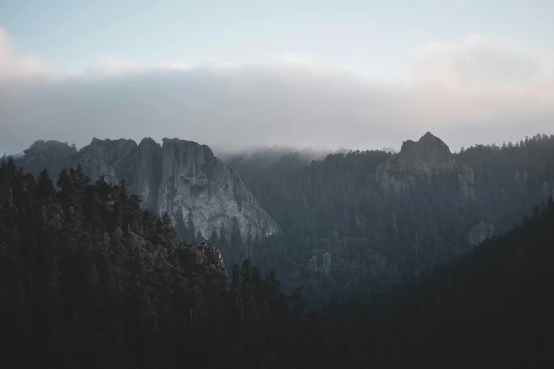 a view of a mountain range with trees in the foreground, by Emma Andijewska, unsplash contest winner, light grey mist, cliff side at dusk, obsidian towers in the distance, minimalistic aesthetics