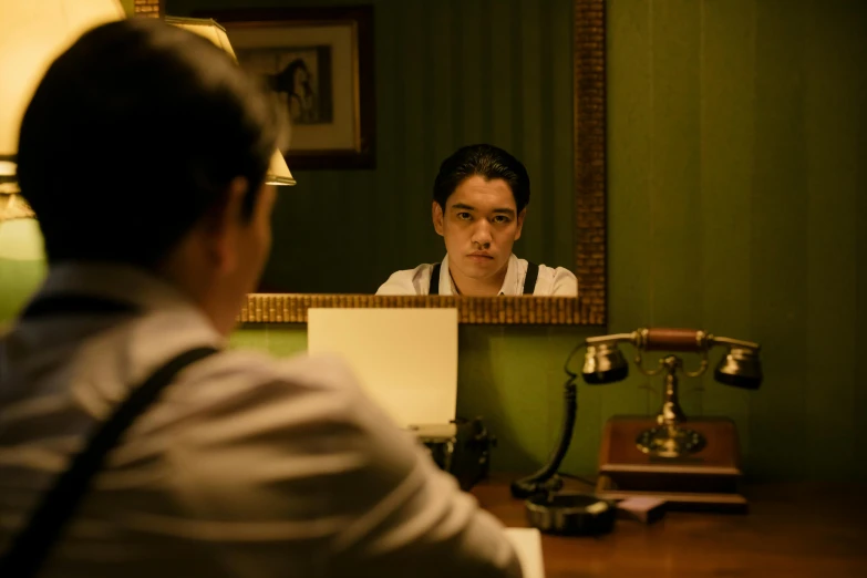 a man sitting at a desk in front of a mirror, inspired by Hideyuki Kikuchi, cinema still, speakeasy, front facing shot, hotel room