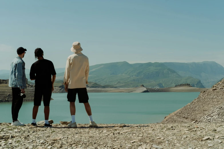 three men standing in front of a body of water, by Muggur, pexels contest winner, hurufiyya, still from a music video, geology, streetwear, georgic