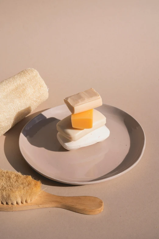 a white plate topped with a piece of cheese next to a brush, inspired by Sarah Lucas, unsplash, modernism, sliced bread in slots, marshmallow graham cracker, soft smooth skin, floating away