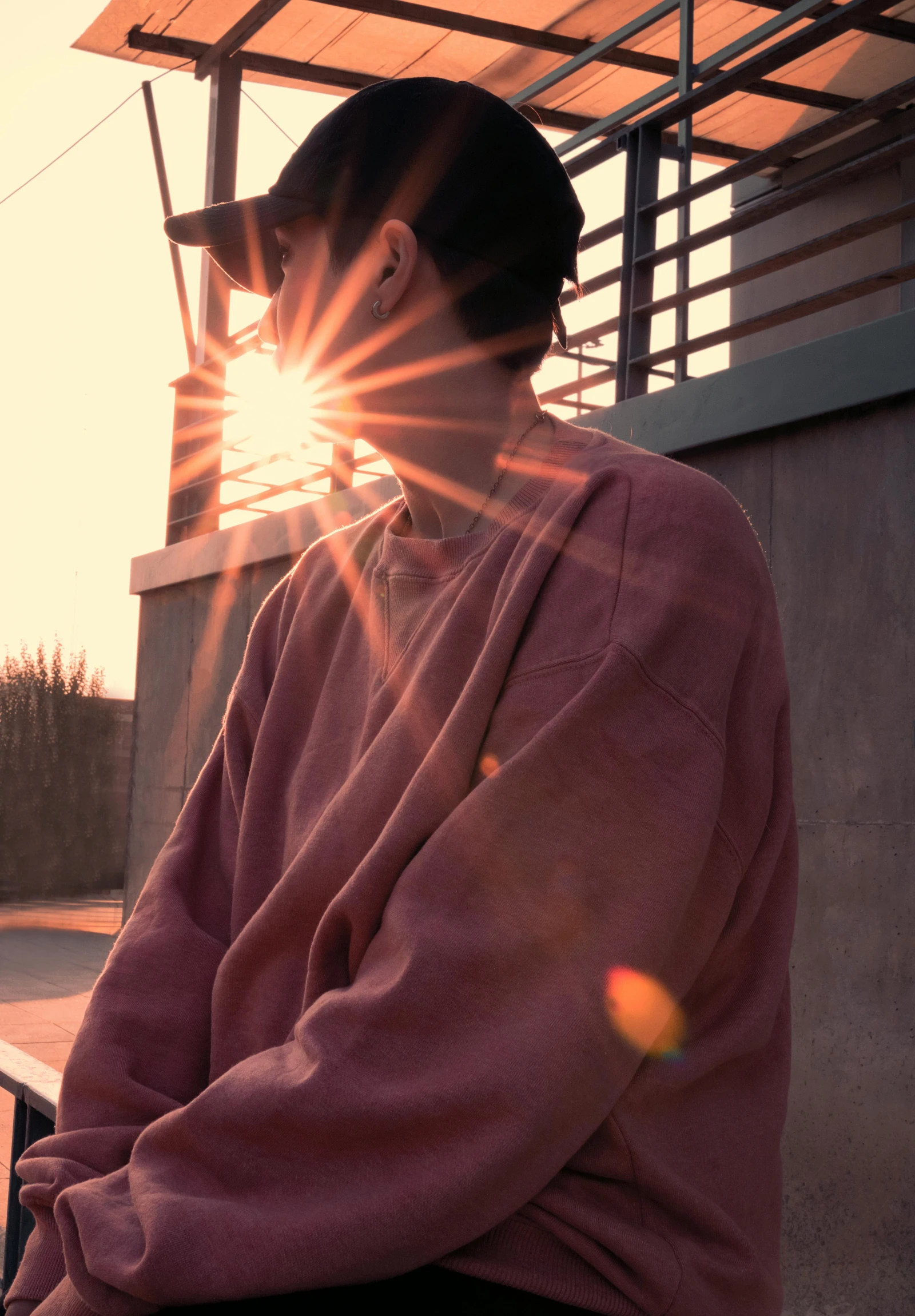 a man sitting on a bench watching the sun go down, inspired by Elsa Bleda, trending on pexels, happening, wearing an oversized sweater, faded pink, standing under a beam of light, male ulzzang