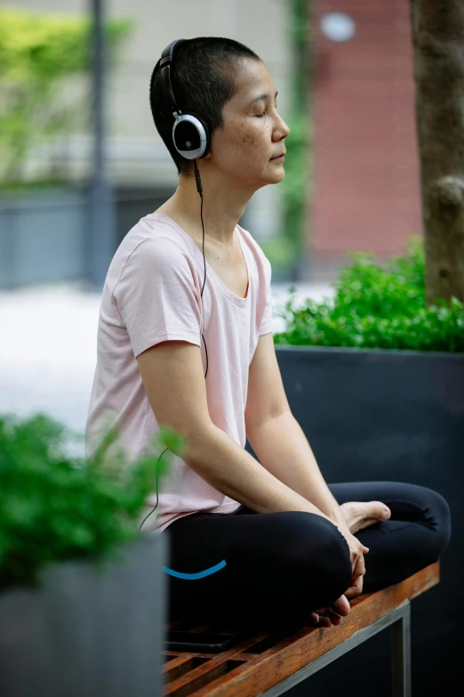 a woman sitting on a bench with headphones on, happening, chi-gong, head turned, wearing fitness gear, in detail