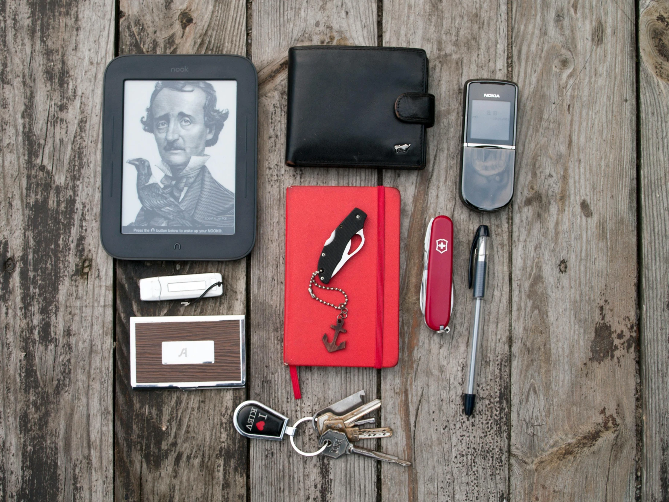 an assortment of personal items laid out on a wooden table, inspired by Evaline Ness, unsplash, happening, black steel with red trim, gigachad portrait, george orwell, handheld