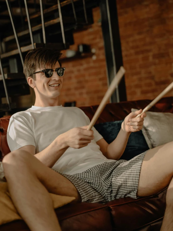 a man sitting on a couch playing drums, by Adam Marczyński, trending on reddit, boy shorts, holding a thick staff, non binary model, profile image