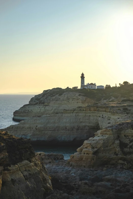 a lighthouse sitting on top of a cliff next to the ocean, beachfront, southern european scenery, warmly lit