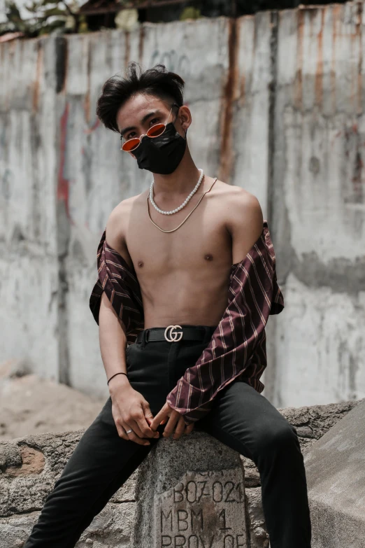 a man sitting on a rock wearing a mask, an album cover, inspired by Hedi Xandt, trending on pexels, graffiti, beads cross onbare chest, male ulzzang, lgbt, gucci clothes