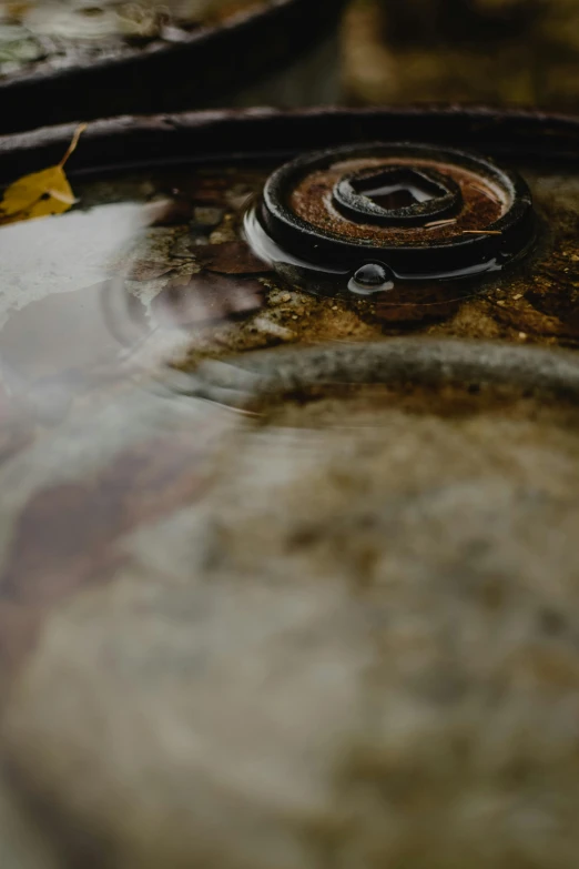 a close up of a metal object in a body of water, an album cover, trending on unsplash, process art, rusty components, large black kettle on hearth, round format, detailed texture
