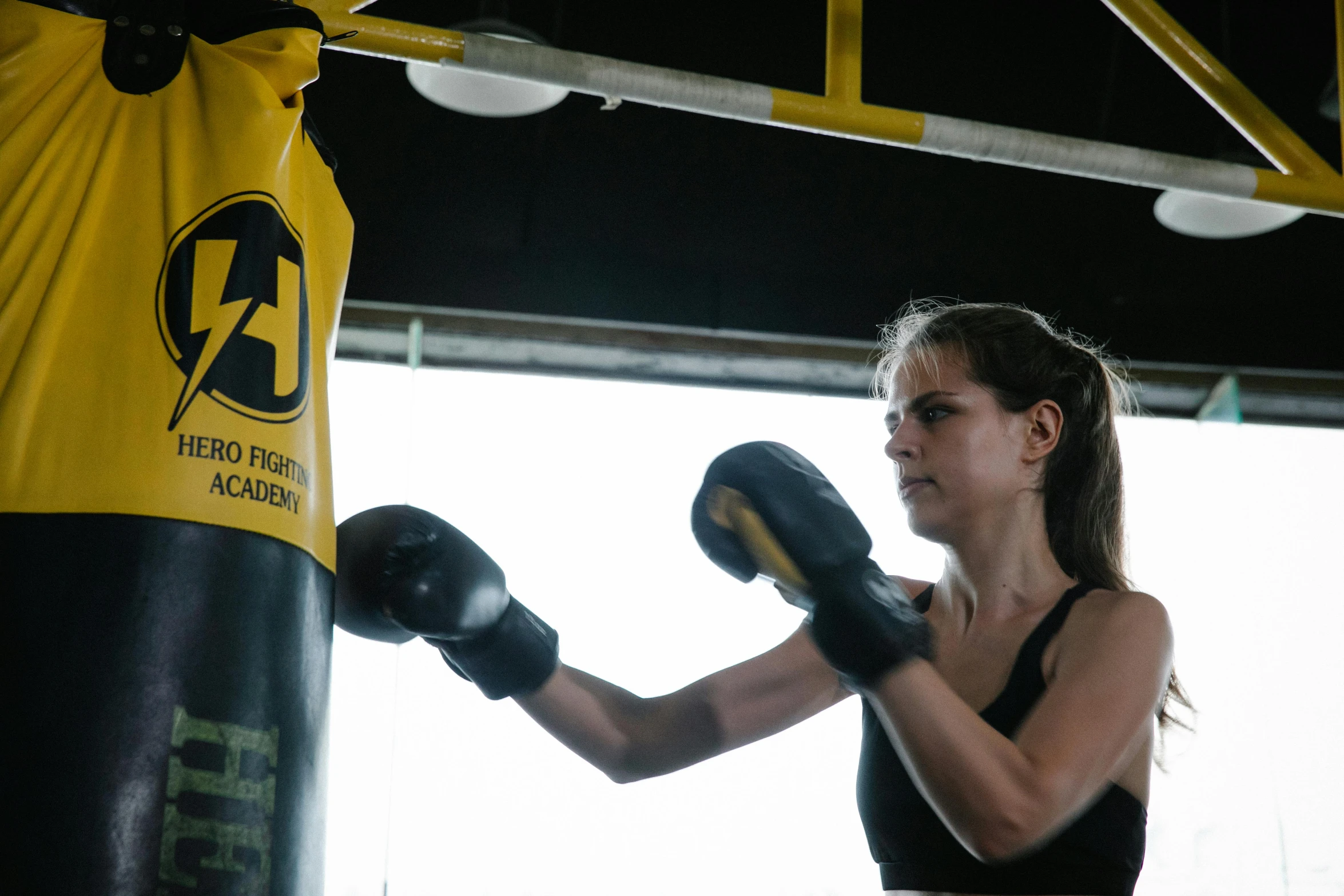 a woman standing next to a punching bag, by Arabella Rankin, pexels contest winner, black and yellow scheme, lifting weights, manuka, profile image