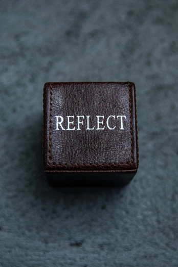 a ring with the word reflect on it, by Nina Hamnett, unsplash, hyperrealism, leather jewelry, solid cube of light, detailed product image, brown