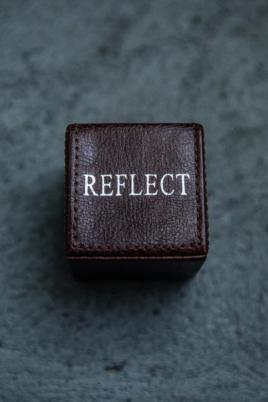 a ring with the word reflect on it, by Nina Hamnett, unsplash, hyperrealism, leather jewelry, solid cube of light, detailed product image, brown