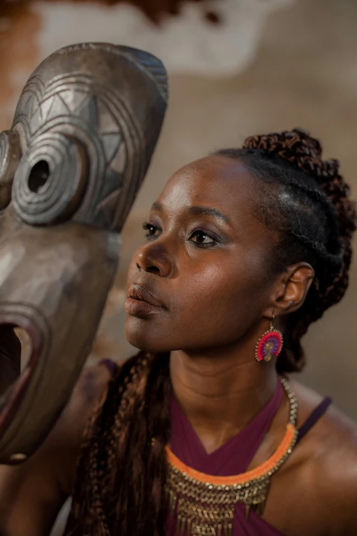 a woman standing next to a wooden mask, inspired by Afewerk Tekle, pexels contest winner, afrofuturism, lupita nyong'o, sitting down, headshot, light-brown skin