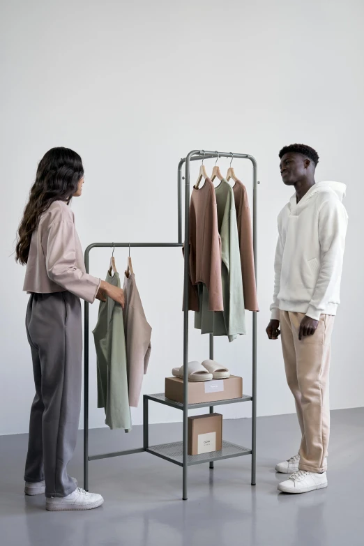 a man and a woman standing in front of a clothing rack, muted colors with minimalism, innovative product concepts, on display, eora