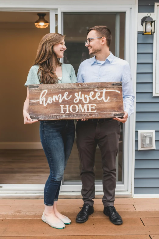 a man and woman standing in front of a house holding a sign, trending on unsplash, fullbody photo, sweet home, close - up studio photo, billboard image