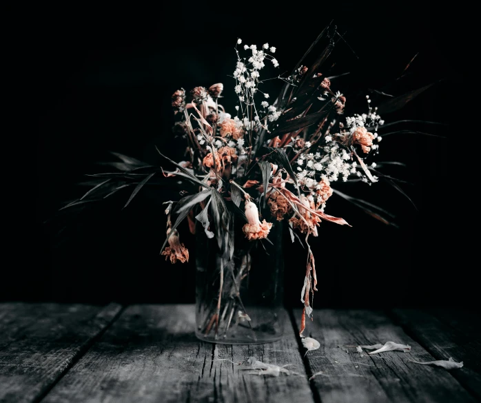 a vase filled with flowers sitting on top of a wooden table, inspired by Elsa Bleda, unsplash, vanitas, dark grey and orange colours, dead plants, black and white colors, nebulous bouquets