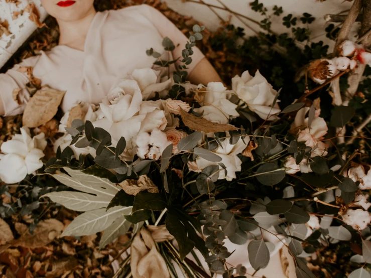 a woman laying on the ground surrounded by flowers, by Emma Andijewska, trending on unsplash, romanticism, magnolia leaves and stems, bouquet, southern gothic art, eucalyptus