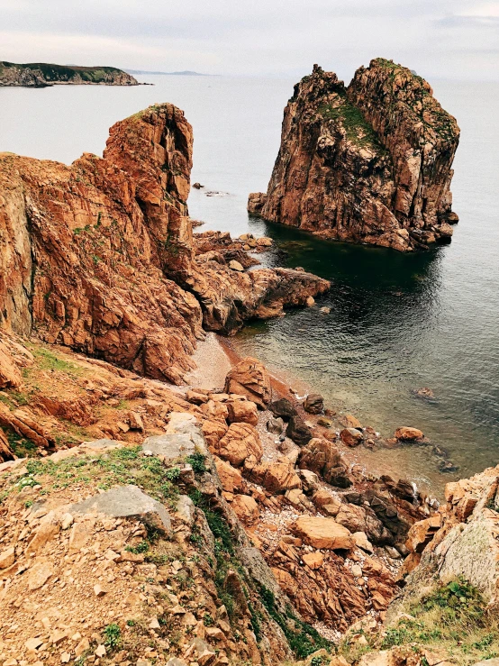 a man standing on top of a cliff next to a body of water, orange rocks, hziulquoigmnzhah, phone photo, overview