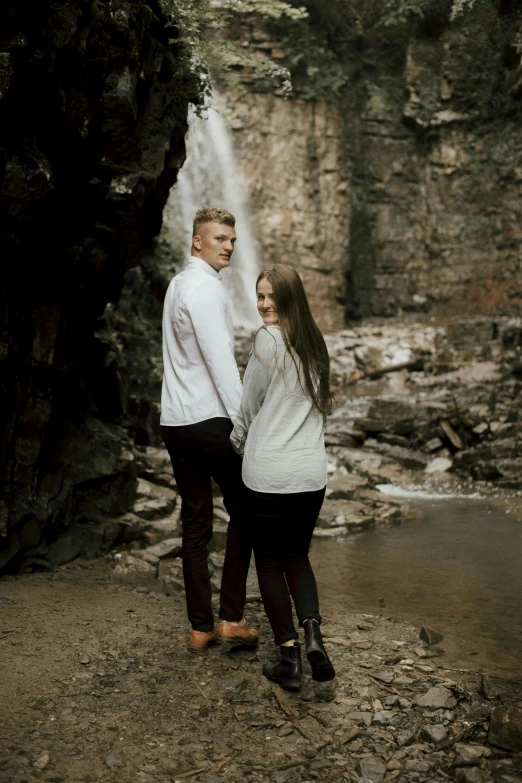 a man and woman standing in front of a waterfall, candid photography, standing on rocky ground, tall forehead, minn