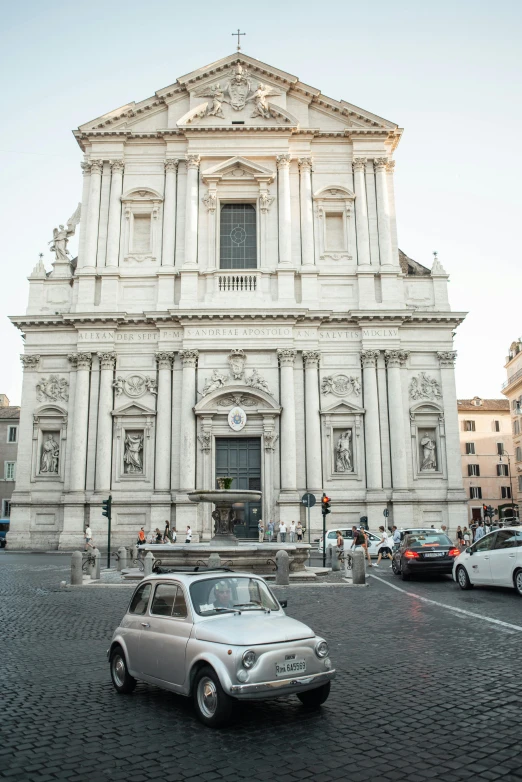 a small car is parked in front of a church, inspired by Giovanni Paolo Pannini, neoclassicism, busy streets, 2019 trending photo, putti, on a great neoclassical square