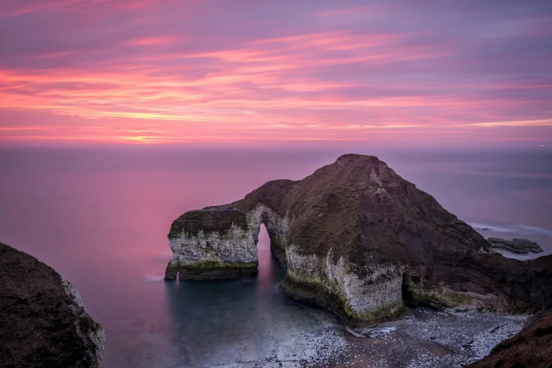 a rock formation in the middle of a body of water, by Andrew Geddes, pexels contest winner, romanticism, pink arches, marsden, godrays at sunset, coastal cliffs