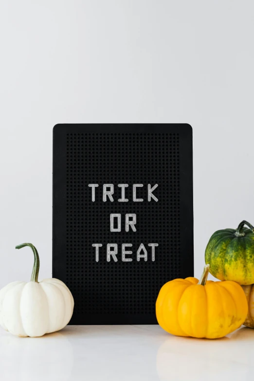 a sign that says trick or treat next to pumpkins and gourds, a poster, by Carey Morris, pexels, ascii art, detail shot, minimalistic aesthetics, panel of black, do