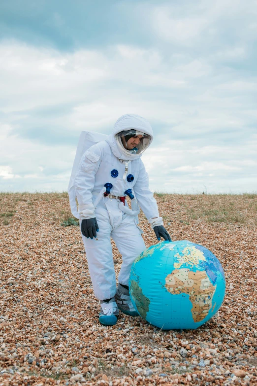 a man in a white space suit standing next to a blue globe, beaching, standing in a barren field, space themed, spacehip lands