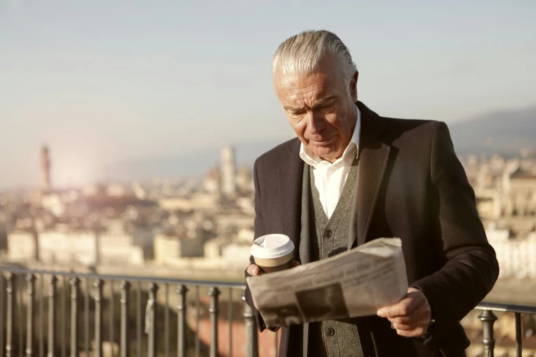 a man reading a newspaper while holding a cup of coffee, a picture, happening, with a city in the background, dark grey haired man, profile image, a man wearing a black jacket