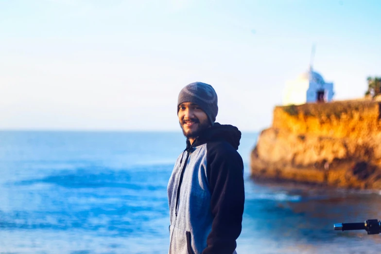 a man standing on top of a beach next to the ocean, a picture, inspired by Abdullah Gërguri, pexels contest winner, les nabis, smiling at camera, san francisco, profile image, background image