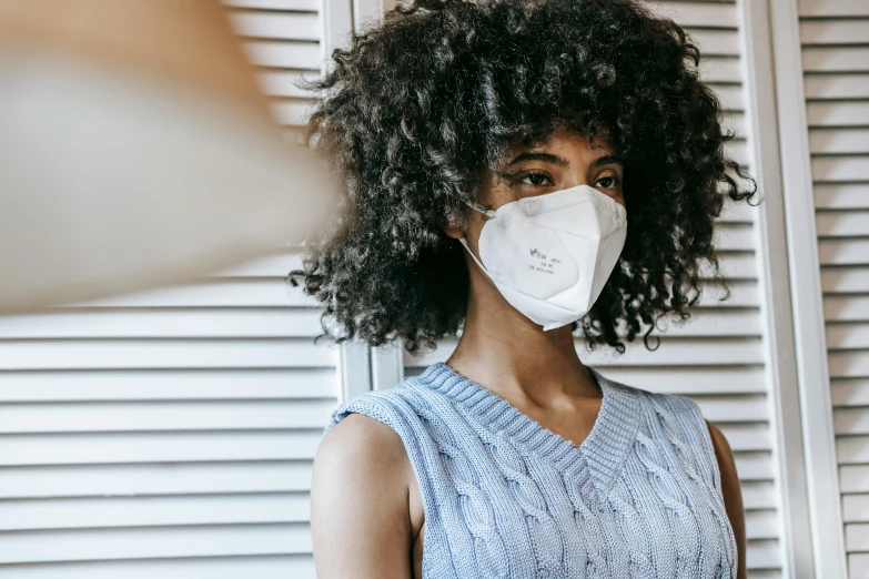 a woman wearing a face mask, by Nicolette Macnamara, trending on pexels, with afro, background image, puff sleeves, grey