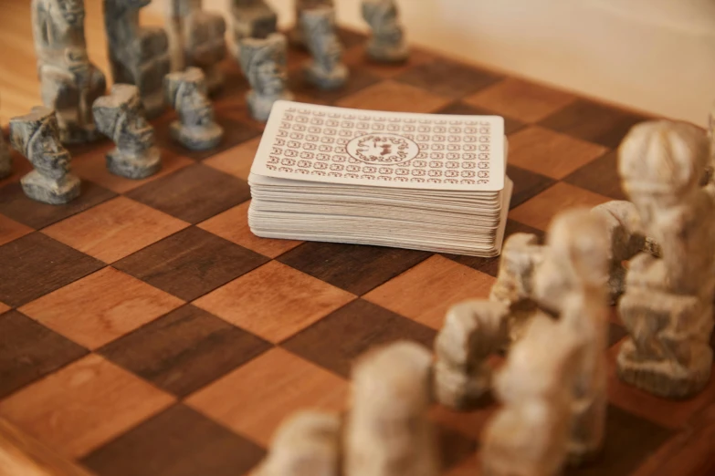 a pile of cards sitting on top of a chess board, inspired by Xuande Emperor, private press, handcrafted, thumbnail, tight shot, at home