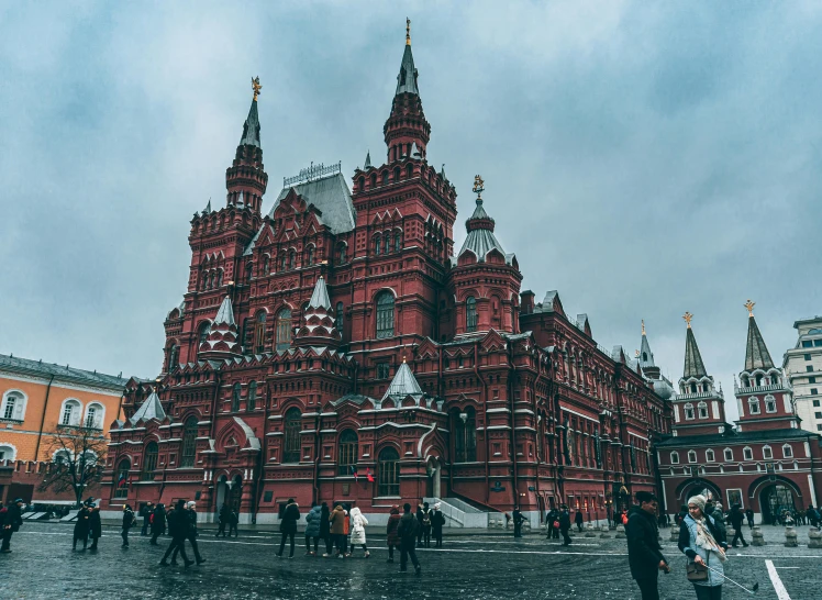 a group of people standing in front of a red building, inspired by Vasily Surikov, pexels contest winner, socialist realism, gothic architecture, on a cloudy day, square, 000 — википедия