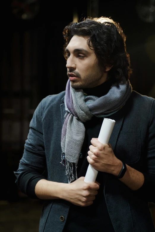 a man holding a roll of paper in his hand, an album cover, inspired by Carlo Mense, pexels contest winner, robert sheehan, scarf, studious chiaroscuro, arab