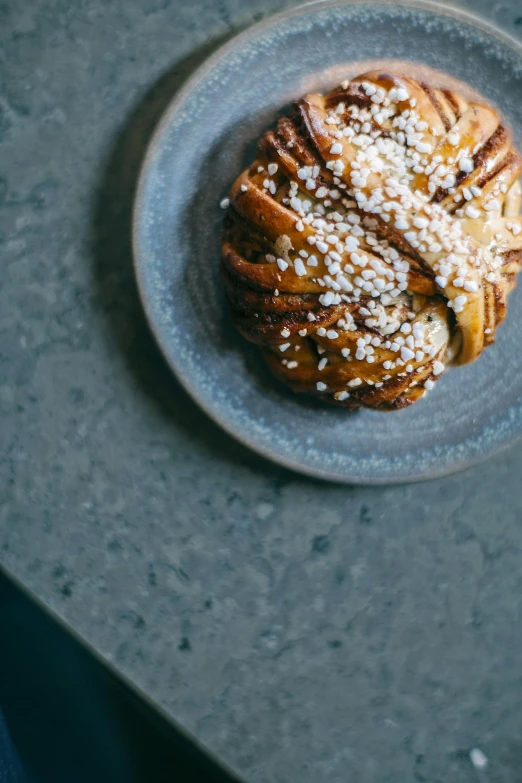 a blue plate topped with a pastry covered in powdered sugar, a portrait, unsplash, alvar aalto, twisted braids, caramel, granite