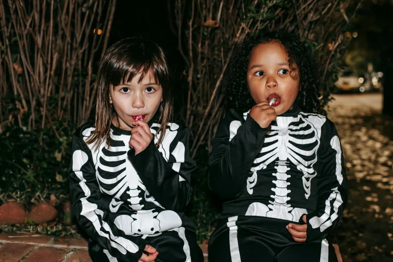 two little girls dressed up in skeleton costumes, a cartoon, by Nina Hamnett, pexels contest winner, wearing a tracksuit, eating, dark-skinned, instagram picture