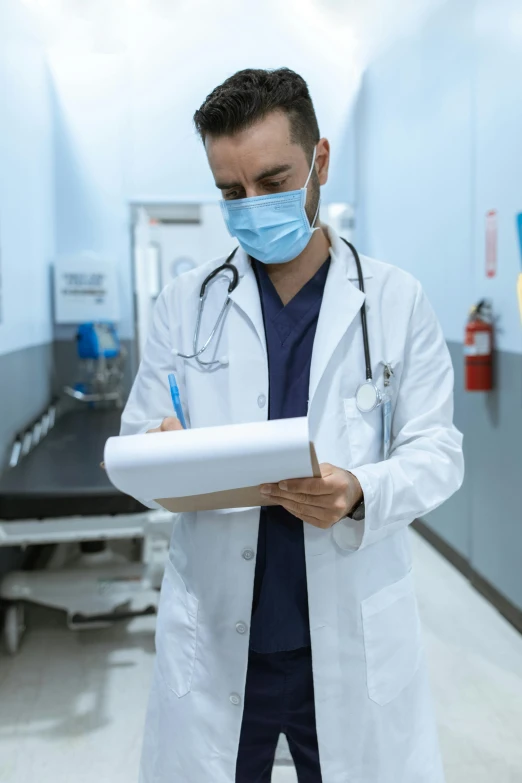 a man in a lab coat and face mask writing on a piece of paper, a picture, shutterstock, emergency room, lgbtq, album photo, a wooden