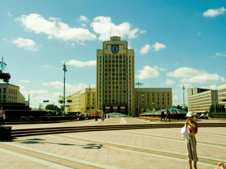 a woman standing in front of a building with a clock tower in the background, unsplash, socialist realism, kazakh, monorail station, 2 0 0 4 photograph, square