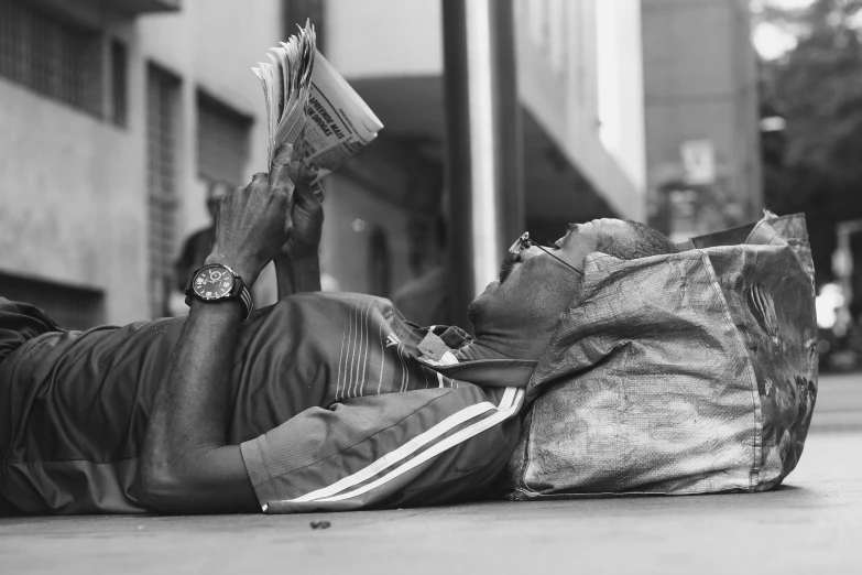 a man laying on the ground reading a book, a black and white photo, by Matija Jama, pexels contest winner, street art, african man, flaunting his wealth, morning time, florida man