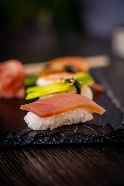 a black plate topped with sushi on top of a wooden table, michelin starred restaurant, square, high-quality photo, pastel'