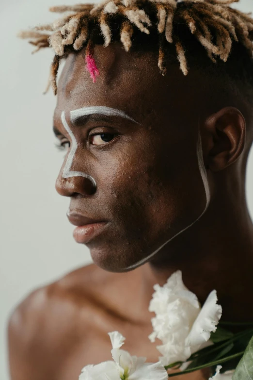 a man with a flower in his hair, by Lily Delissa Joseph, trending on pexels, afrofuturism, white face paint, nonbinary model, side portrait of elven royalty, a young man