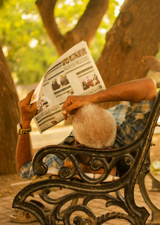 a man sitting on a bench reading a newspaper, a picture, pexels contest winner, private press, at khajuraho, relaxed dwarf with white hair, reading under a tree, resting head on hands