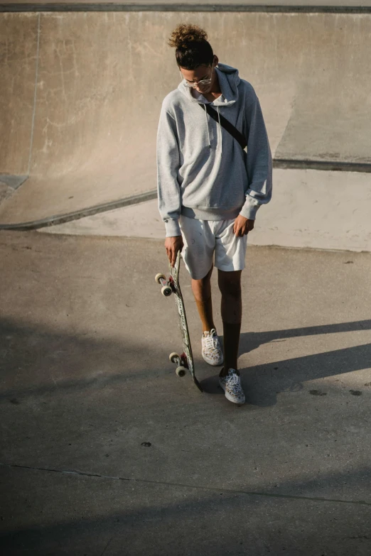 a man holding a skateboard in a skate park, a picture, trending on unsplash, white fluffy cotton shorts, grey hoodie, soft shadow transition, 1 2 9 7