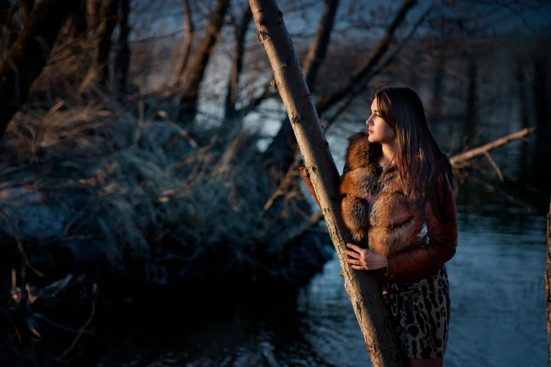 a woman standing next to a tree near a body of water, a portrait, inspired by Elsa Bleda, pexels contest winner, renaissance, real fur and real skin, hunting, evening lighting, brown