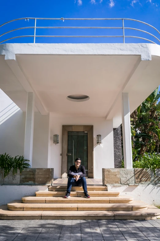 a man sitting on the steps of a house, inspired by Ricardo Bofill, unsplash, modernism, wide angle full body, puerto rico, portrait of a mark zuckerberg, mansion