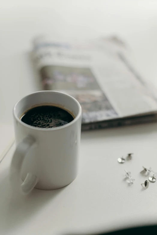 a cup of coffee sitting on top of a table, private press, with sparkling gems on top, newspaper, on a white table, promo image