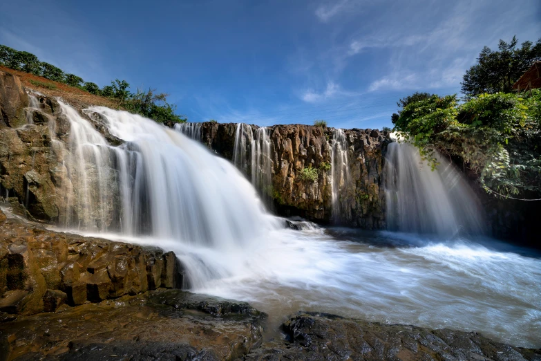 a large waterfall in the middle of a forest, by Reuben Tam, unsplash, hurufiyya, blue sky, madagascar, water running down the walls, thumbnail