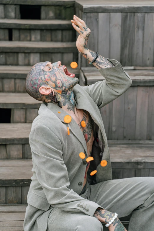 a man in a suit sitting on some steps, a tattoo, inspired by Hendrik Goltzius, trending on pexels, renaissance, extreme face contortion, confetti, muscular body tattooed, grey suit