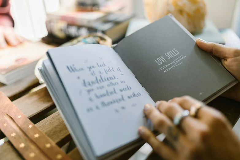 a close up of a person holding a book, pexels contest winner, letterism, 9 9 designs, notebook, grey, family friendly