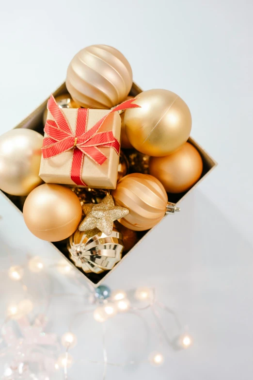 a box filled with christmas ornaments sitting on top of a table, a still life, pexels, golden color scheme, brightly lit!, tan, set against a white background