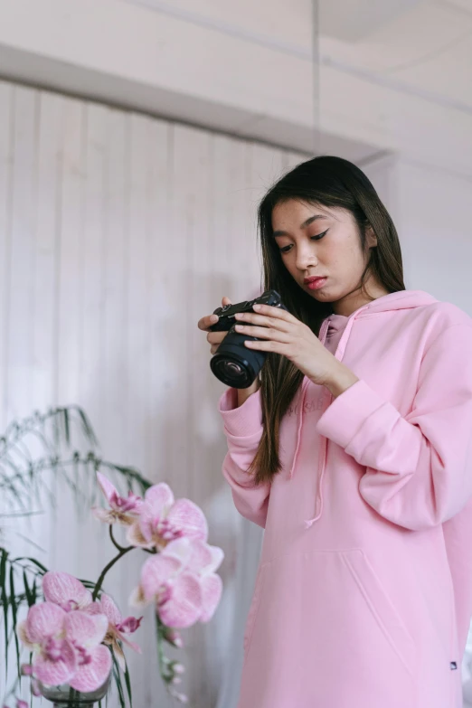 a woman in a pink hoodie taking a picture with a camera, trending on pexels, mai anh tran, at home, portrait sophie mudd, aesthetic!!